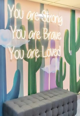 Tufted bench in front of an art-panel wall with an inspirational phrase neon sign.