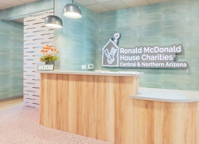 Ronald McDonald House reception area with wooden desk, pendant lights, and neon logo sign on the wall.