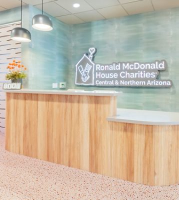Ronald McDonald House reception area with wooden desk, pendant lights, and neon logo sign on the wall.