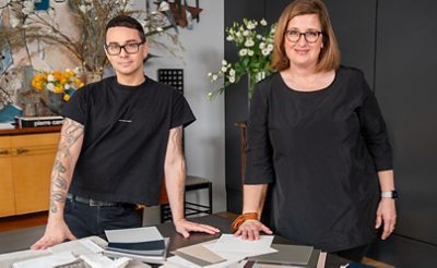 Christian Siriano and Sue Wadden, both dressed in black, standing at a table covered in paint samples in Siriano’s home.
