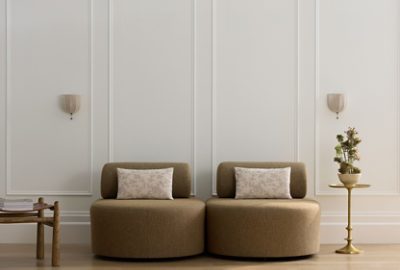 A chic sitting area with two round beige chairs, accent pillows, side tables, and small sconces against a paneled wall painted in Sherwin-Williams White Snow.