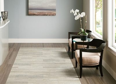 A waiting room with a reception desk, vinyl plank flooring with a rug, two chairs with a round table with a flower and large bright windows.