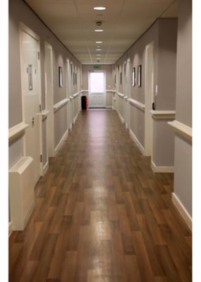 A long hallway of a nursing room facility with vinyl plank flooring.