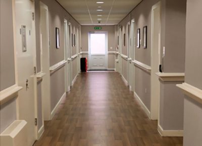 A long hallway of a nursing room facility with vinyl plank flooring.