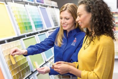 Two people selecting paint samples in front of a Sherwin-Williams color display.