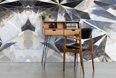 A small modern writing table against a wall with bold, geometric printed wallpaper.