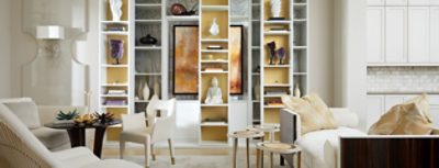 White living room with custom built-in shelving focal point displaying stacked books, pottery, and art pieces.