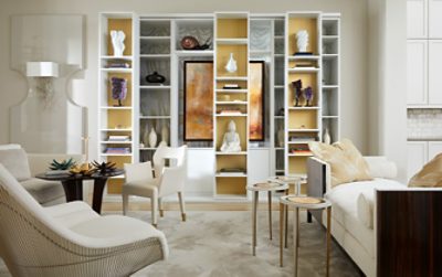 White living room with custom built-in shelving focal point displaying stacked books, pottery, and art pieces.