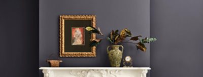 A white mantel with a decorative vase, framed artwork, a clock, and a small basket against walls painted Sherwin-Williams Midnight.