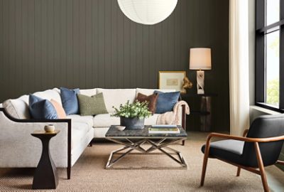 Living room with Sherwin-Williams Roycroft Bronze Green paneled walls, beige sectional sofa with blue, green, and neutral pillows, a metal and marble coffee table, and window with black Sherwin-Williams Caviar frame.