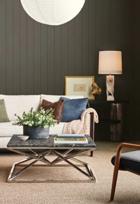 Living room with Sherwin-Williams Roycroft Bronze Green paneled walls, beige sectional sofa with blue, green, and neutral pillows, a metal and marble coffee table, and window with black Sherwin-Williams Caviar frame.