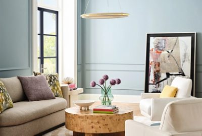 Sherwin-Williams Dutch Tile Blue–painted living room with a sofa and armchairs, round wooden coffee table, French doors painted dark purple using the color Mountain Fig, a White Snow ceiling and trim, and a large abstract art piece leaning against the back wall.
