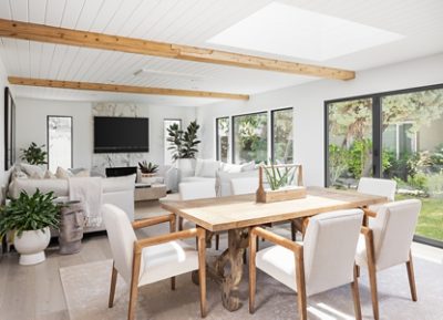 Bright living and dining room with Sherwin-Williams Pure White paint, wooden beams, white sofas, and a wooden dining table, featuring large windows and indoor plants.