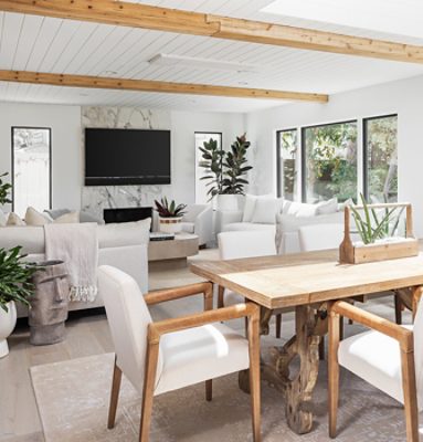 Bright living and dining room with Sherwin-Williams Pure White paint, wooden beams, white sofas, and a wooden dining table, featuring large windows and indoor plants.