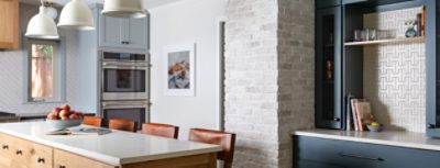 A modern kitchen featuring a light wood island with a bowl of fruit, brown leather chairs, and cabinetry in Sherwin-Williams Mineral Deposit alongside walls in Sherwin-Williams Drift of Mist and a bar in Sherwin-Williams Slate Tile.