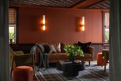 Cozy living room with a brown leather sofa, decorative pillows, and a coffee table topped with flowers, surrounded by warm Sherwin-Williams Cavern Clay walls and soft lighting.