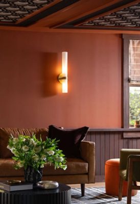 Cozy living room with a brown leather sofa, decorative pillows, and a coffee table topped with flowers, surrounded by warm Sherwin-Williams Cavern Clay walls and soft lighting.