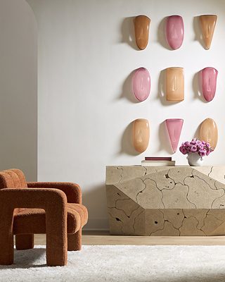 Modern living room with a rust-colored chair, wooden console, pink and peach wall art, and a vase of flowers.