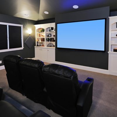 A basement with a large screen in front of a leather couch with dark painted walls.