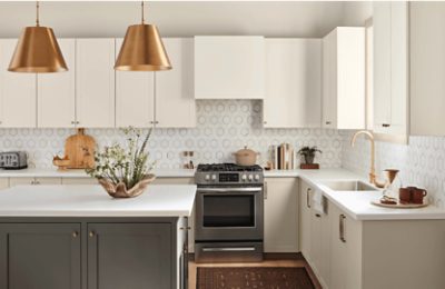 A kitchen with a geometric white and gray tile backsplash with cream cabinets and a gray-green island.