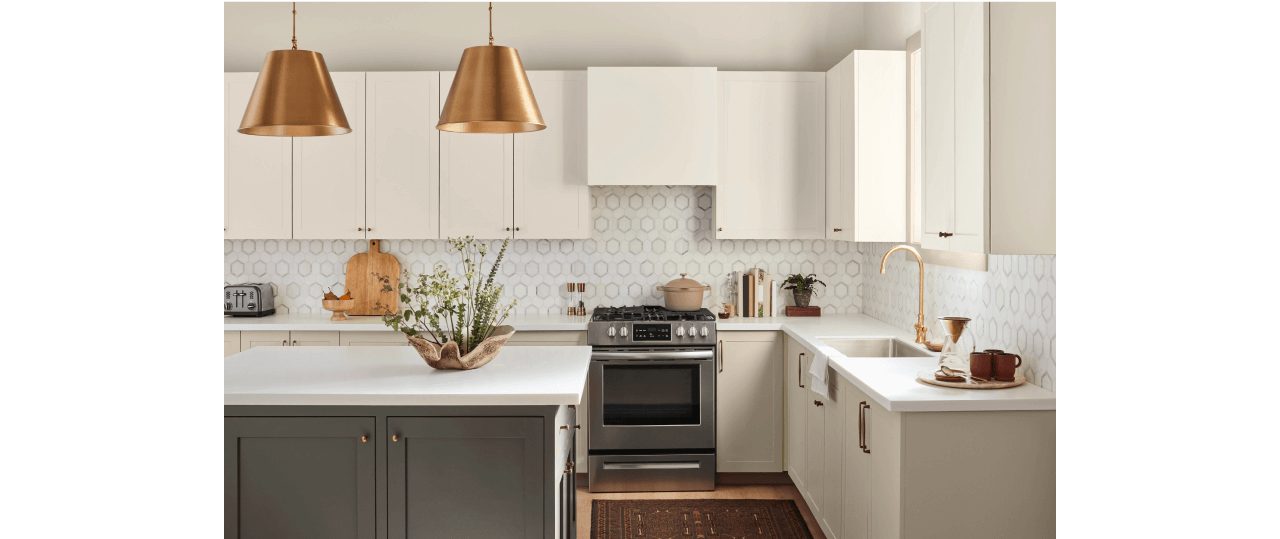 A kitchen with a geometric white and gray tile backsplash with cream cabinets and a gray-green island.