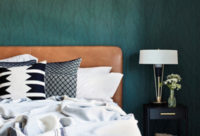 A bed with a tan leather headboard against a rich green wallpaper.