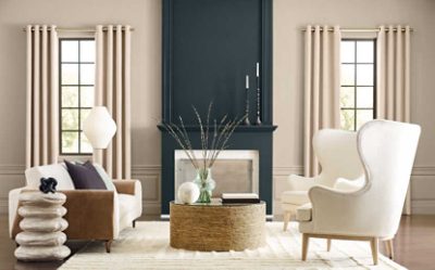 An elegant sitting area with white upholstered furniture and walls painted light tan with a dark fireplace.