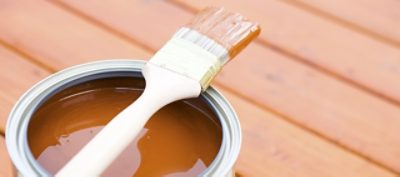 An open gallon of brown deck paint and a paint brush.
