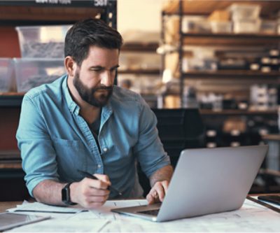 A person at a table taking notes and using a laptop.