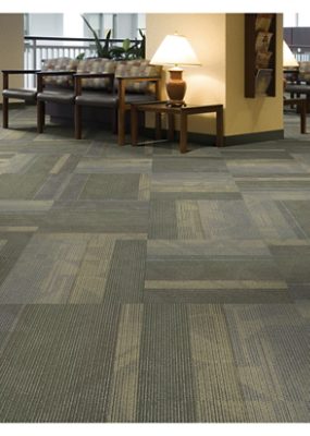 A large waiting room with three chairs and and end table with patterned tile carpet.