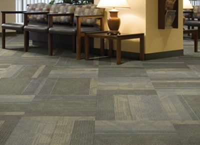 A large waiting room with three chairs and and end table with patterned tile carpet.