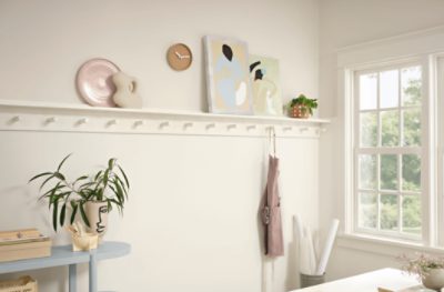 A narrow shelf holding art pieces on a wall painted Alabaster SW 7008.