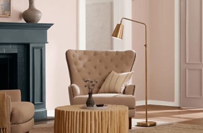 A living room painted SW 6057 Malted Milk, with a circular coffee table, large chair next to a golden floor lamp and fireplace.