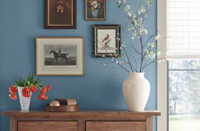 A table with vases in front of four prints hung on a wall painted Smoky Azurite SW 9148.