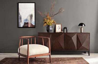 A room painted Urbane Bronze SW 7048, paired with a chair with large white cushion on a rug next to a dark stained dresser.