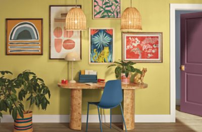 An oval desk against a wall painted in SW 0073 Chartreuse with a collage of prints.