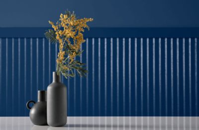 A black vase with yellow flowers in front of a wall painted Commodore SW 6524.