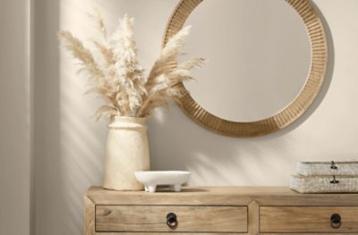 A light wood table with neutral decor against a wall painted Shiitake SW 9173 with a gold round mirror above it.
