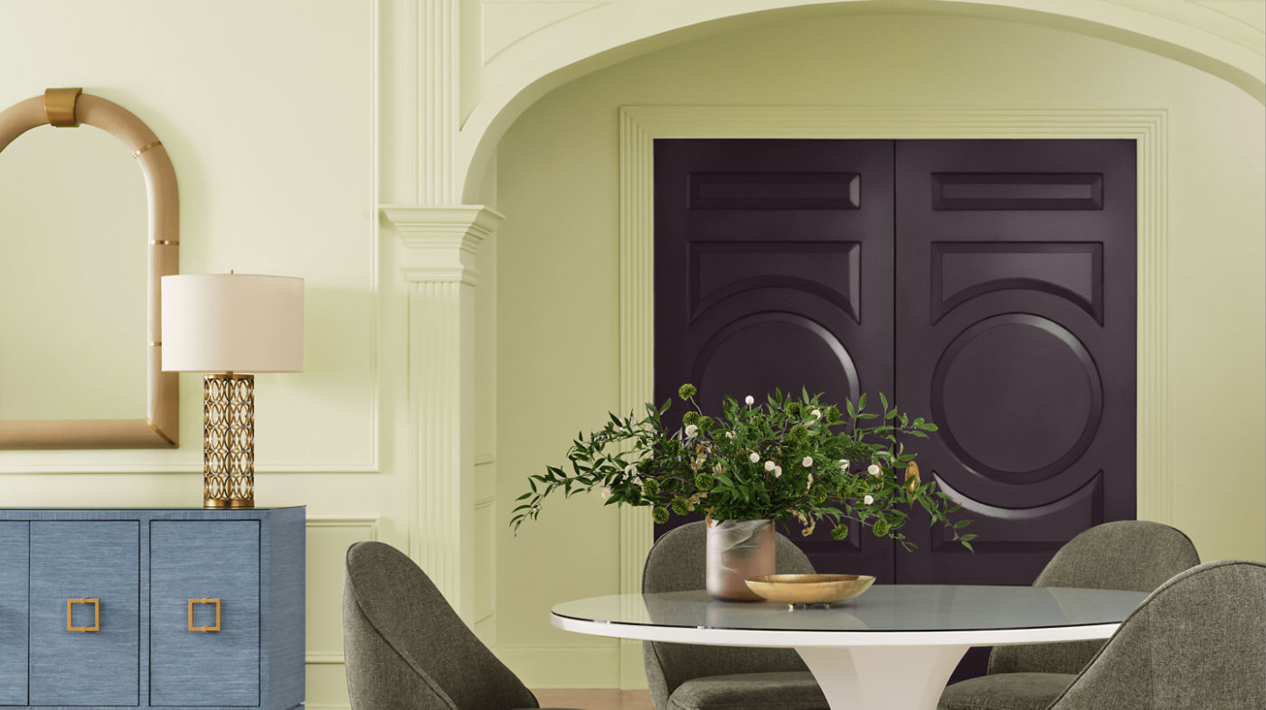 Sala da pranzo con pareti verde chiaro erbaceo, arco e porta color prugna