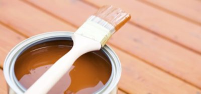 An open gallon of brown deck paint and a paint brush. 