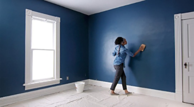 A woman cleaning the surface of a blue wall.