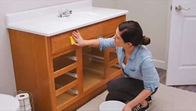 A woman cleaning a bathroom vanity with a sponge.