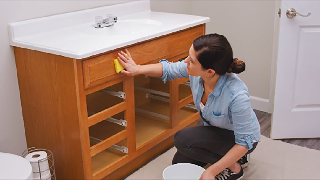 A woman cleaning a bathroom vanity with a sponge.