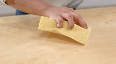 A person cleaning a coffee table with a sponge.