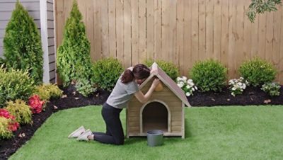 A woman cleaning the exterior of a dog house. 