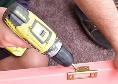 A person's hand using a power drill reattaching brass hardware to a painted closet door.