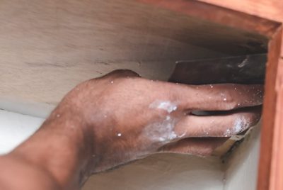 Using a piece of sandpaper to prep the inside of a cabinet for painting.