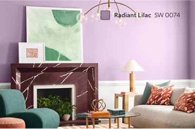 A living room with a purple Radiant Lilac SW 0074 wall, a red marble fireplace, green armchair, orange ottoman, gray sofa with patterned pillows, and a glass coffee table.