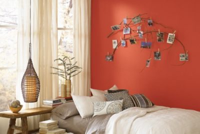 A bedroom with a low bed covered in gray, white and black textiles against a bold orange accent wall.