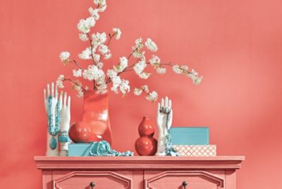 A light red table holding white, red and turquoise decor in front of a light red wall.